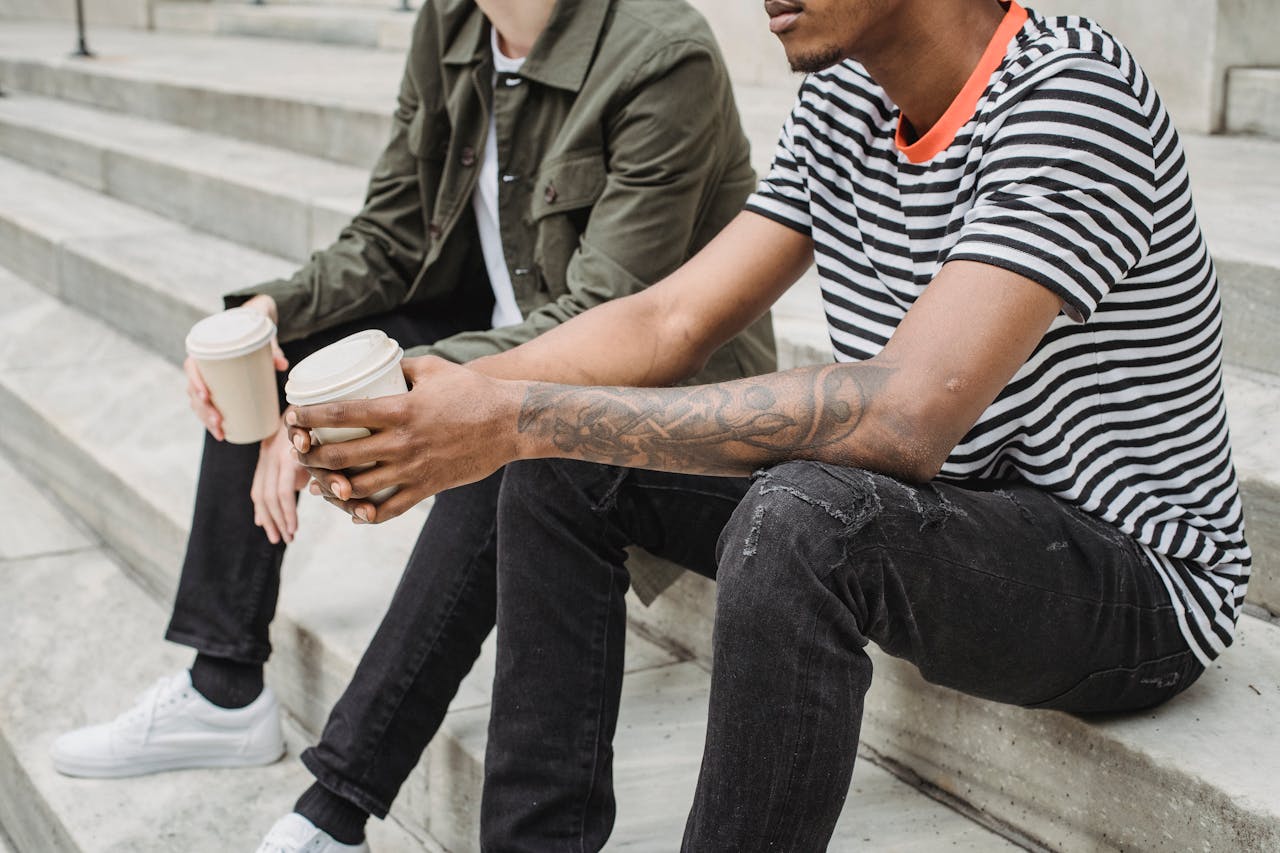 Two men enjoy coffee on city steps, embracing a casual urban lifestyle.